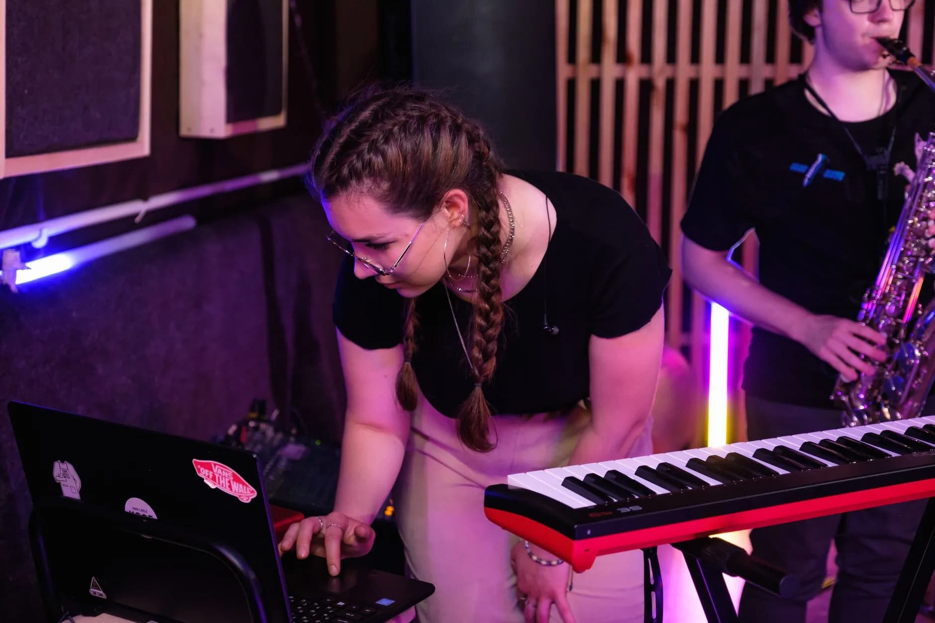 Musicisti che lavorano in uno studio vivace con tastiere e sassofono. Energia creativa e concentrazione.