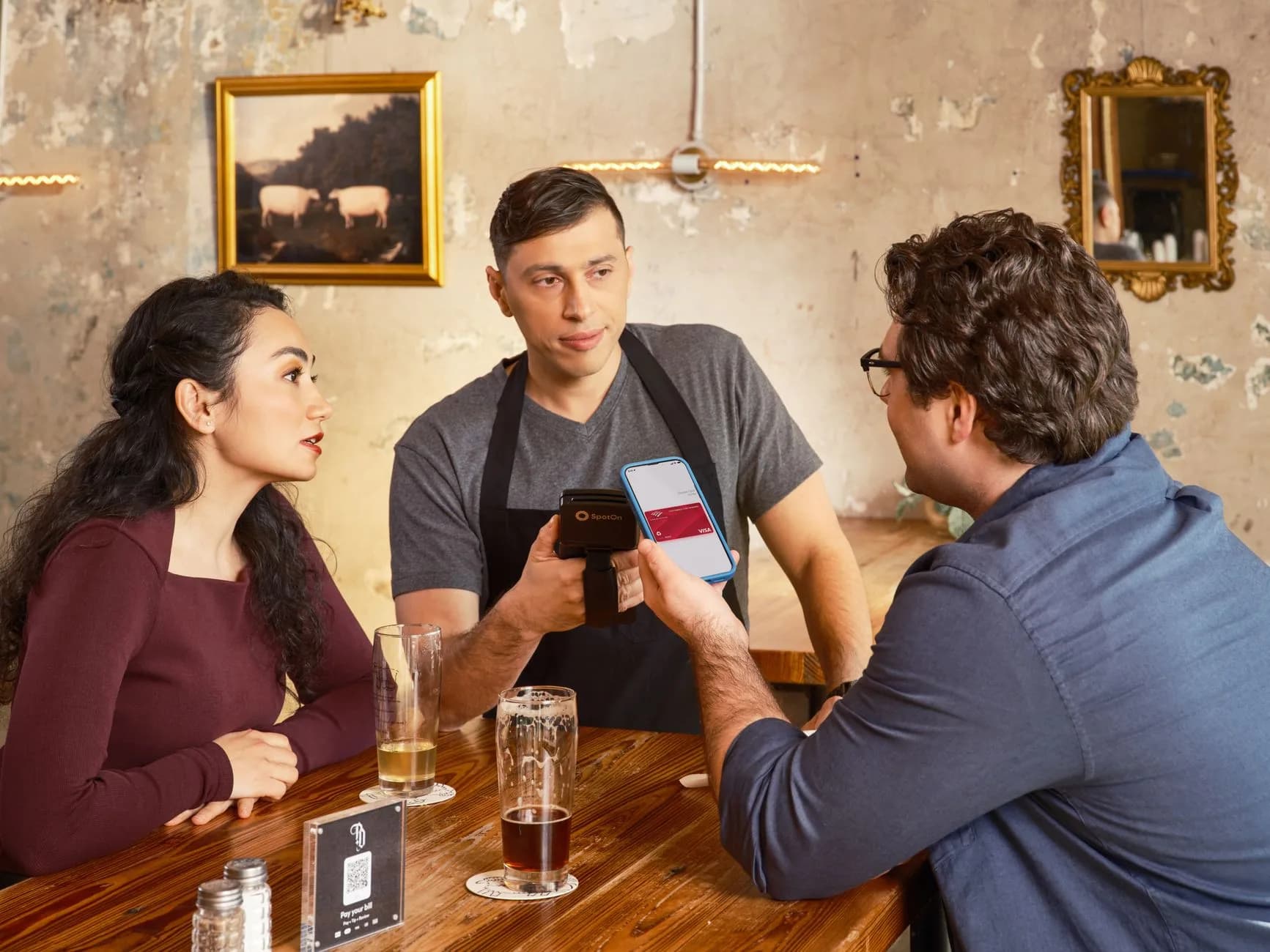 Una coppia effettua un pagamento contactless utilizzando lo smartphone al bancone del bar di un ristorante.