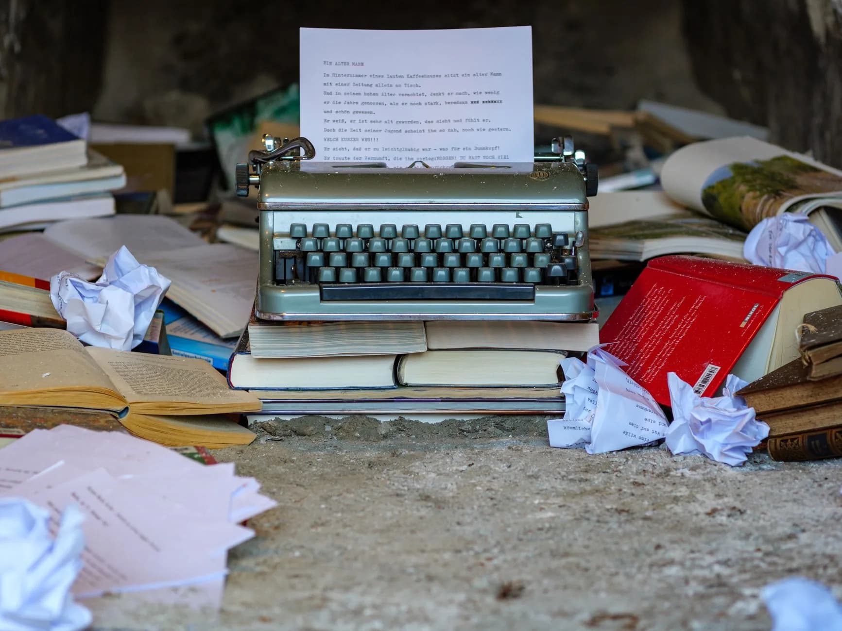 Una macchina da scrivere d'epoca circondata da libri aperti e fogli spiegazzati, simbolo del caos creativo.